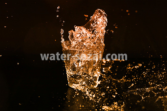 オレンジ色に着色されたロックグラスの水が弾ける写真・フォト素材