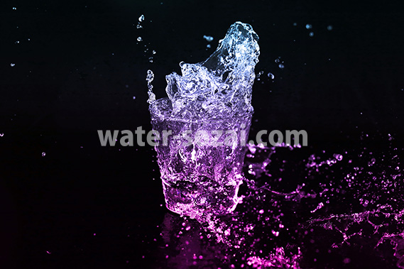 青からピンク色に着色されたロックグラスの水が弾ける写真・フォト