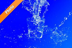 青背景のロックグラスと水が散布する写真・フォト素材