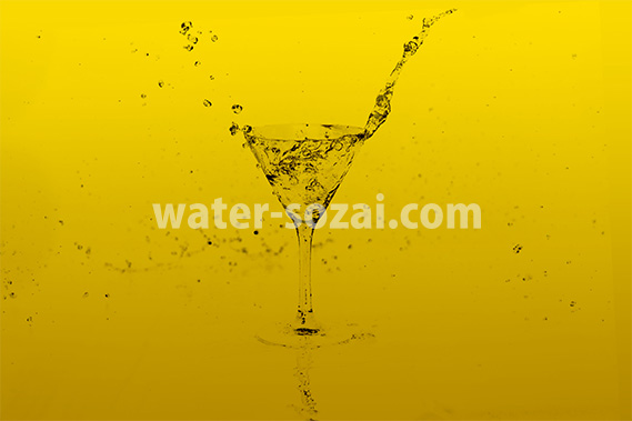 黄色の背景のカクテルグラスと水が弾ける写真・フォト