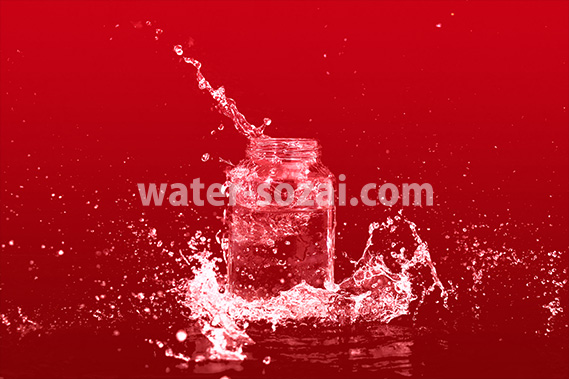 赤い背景のビンと水が飛び散る写真・フォト素材