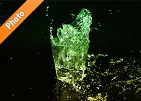 緑色に着色されたロックグラスの水が弾ける写真・フォト素材