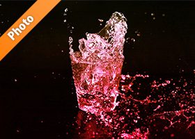 赤色に着色されたロックグラスの水が弾ける写真・フォト素材