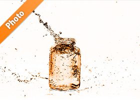 オレンジ色に着色されたビンと水が弾ける写真・フォト素材
